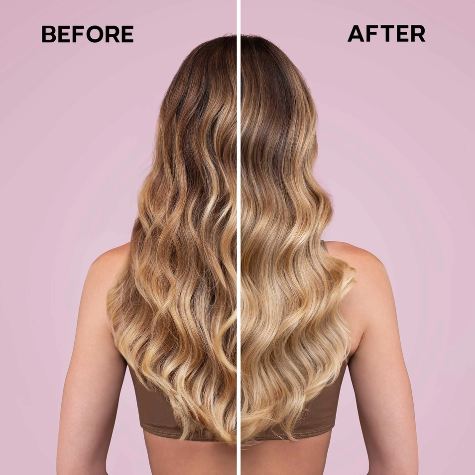 Before and after comparison of a woman's long wavy hair, showing a dark brown root color blending into warm blonde highlights. The model is shown from the back wearing a brown strap top against a solid pink background, with 'BEFORE' and 'AFTER' text labels.